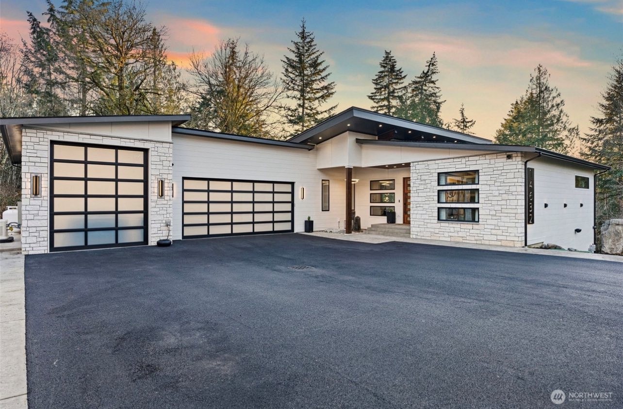 Modern single-story custom home with stone veneer and glass garage doors at twilight