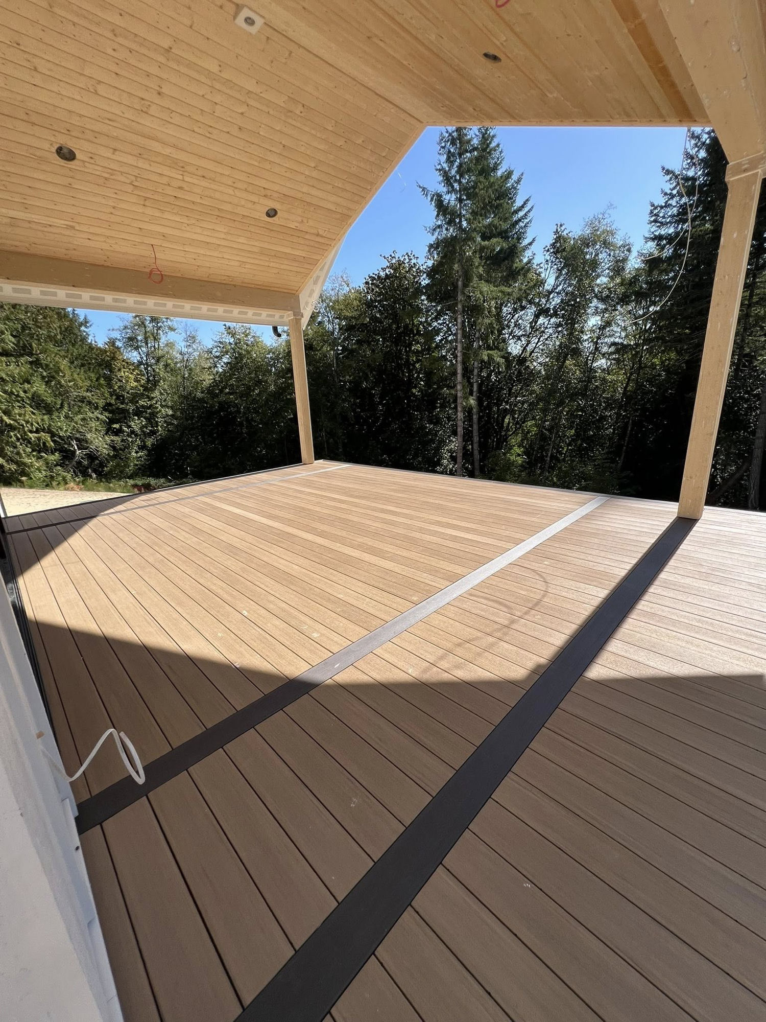 Covered composite deck with tongue-and-groove cedar ceiling surrounded by evergreen trees